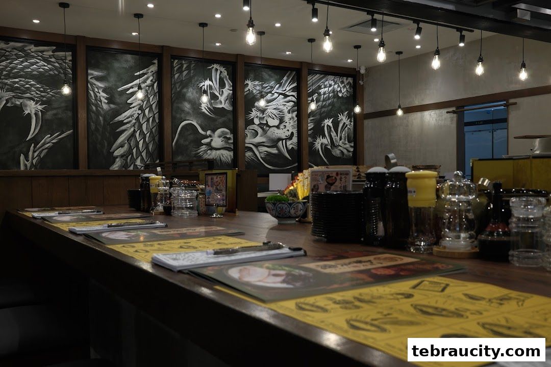 A ramen shop counter with dragon artwork on the wall and menus on the table.