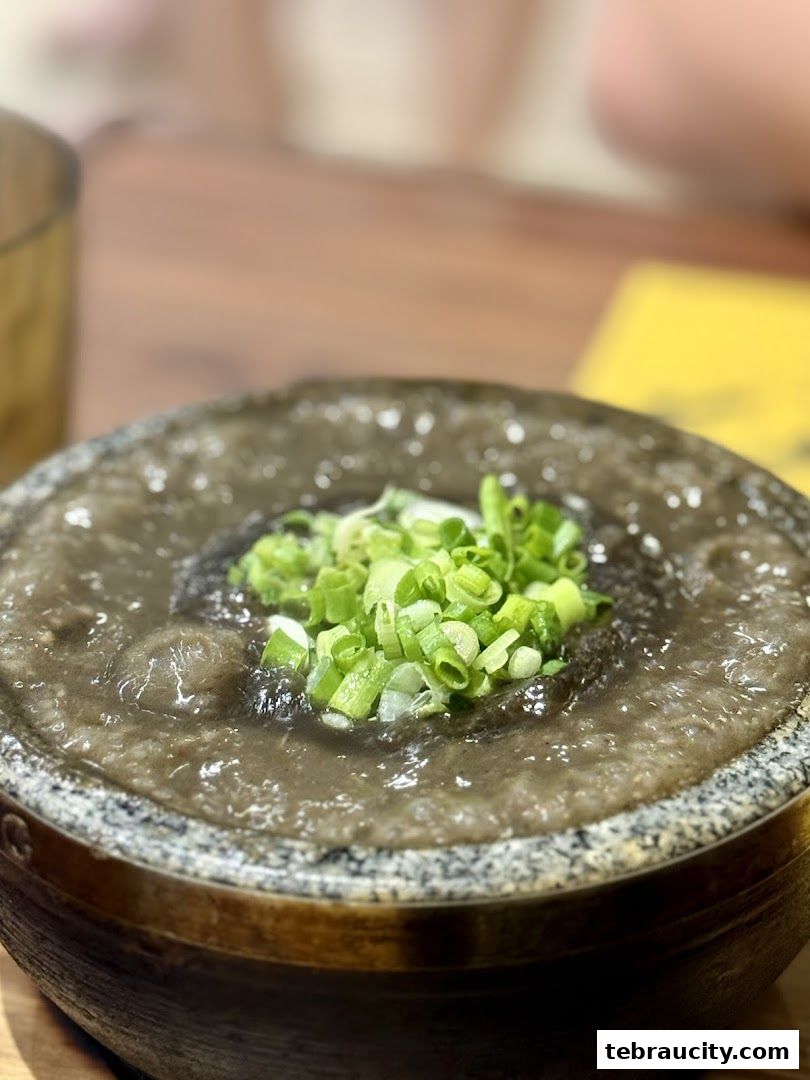 A close-up of a stone bowl filled with dark ramen broth and topped with chopped green onions.