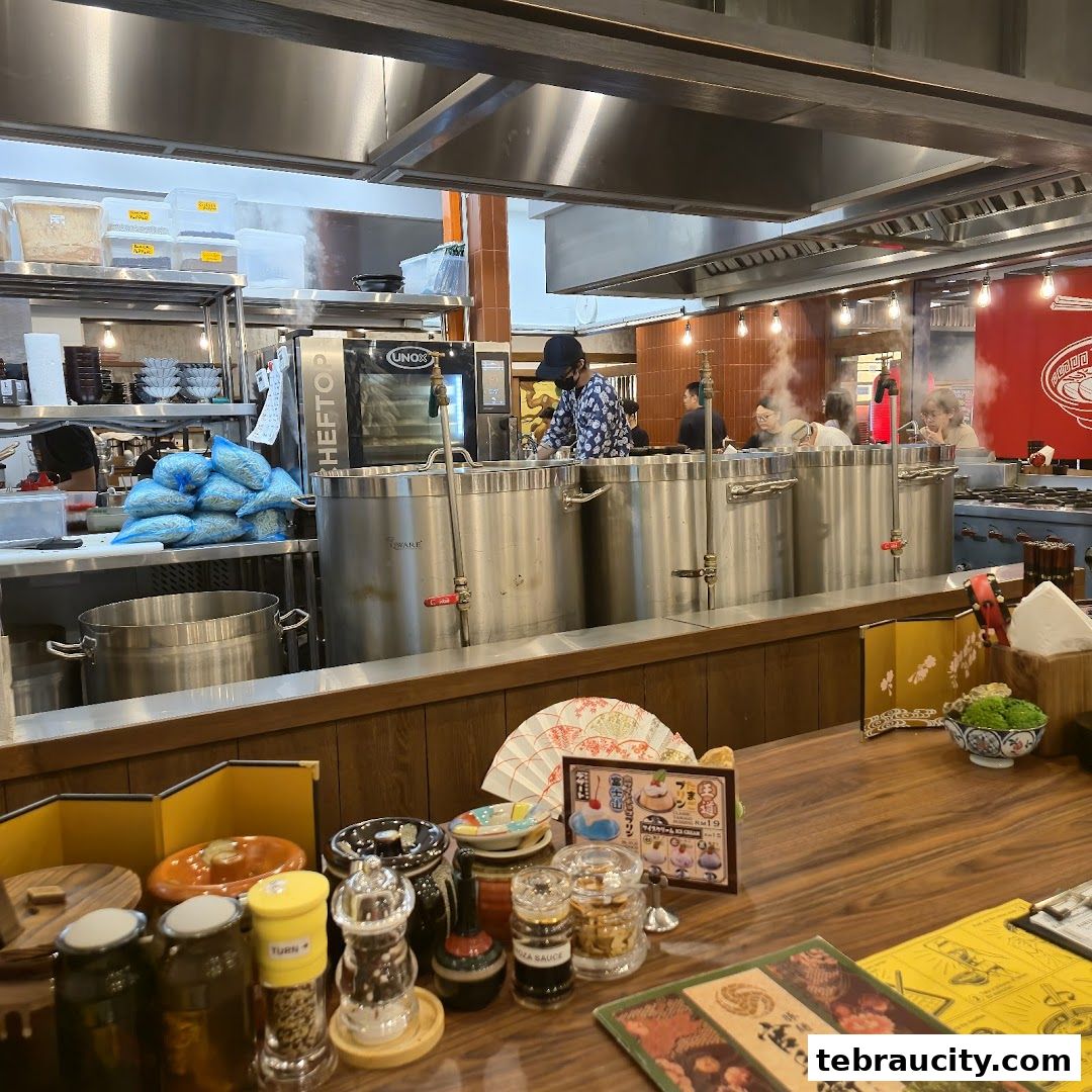 A busy ramen shop kitchen with chefs preparing food and customers dining.