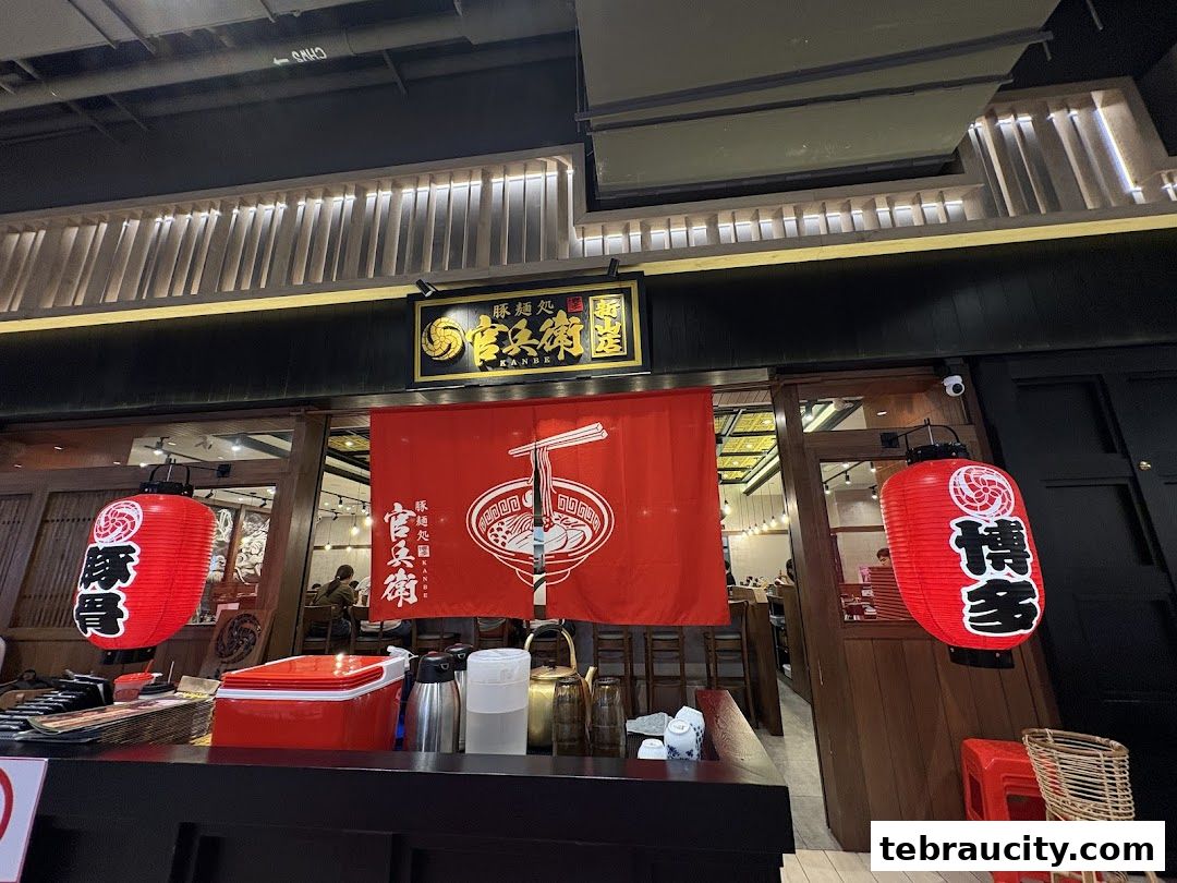 The entrance of a ramen shop with red lanterns and a noren curtain.