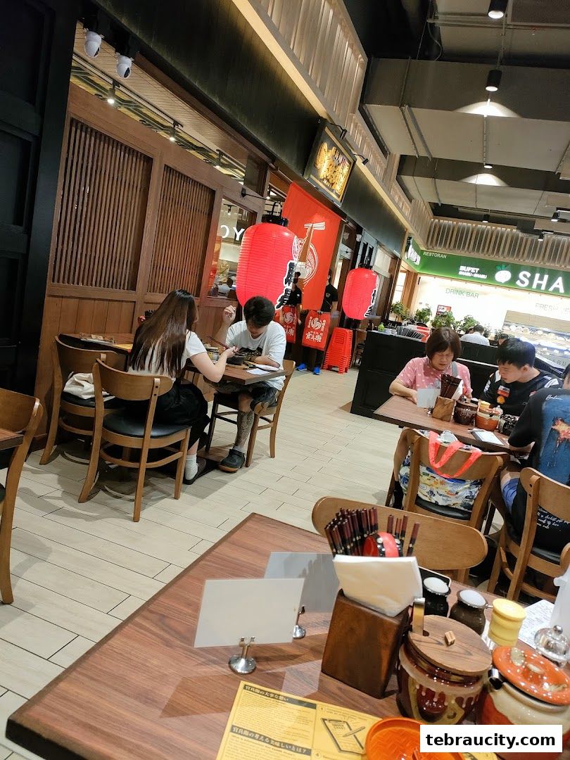 Diners enjoy ramen at tables inside a Japanese restaurant with red lanterns.