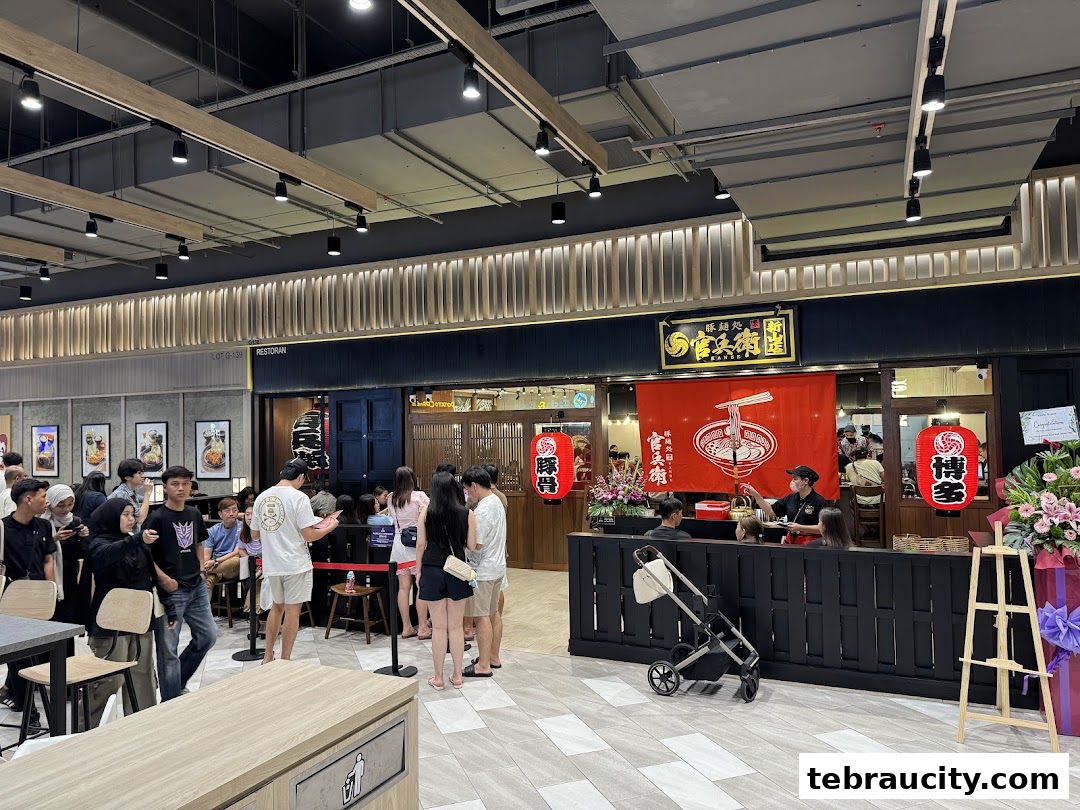 A busy ramen shop with customers queuing outside and staff serving inside.