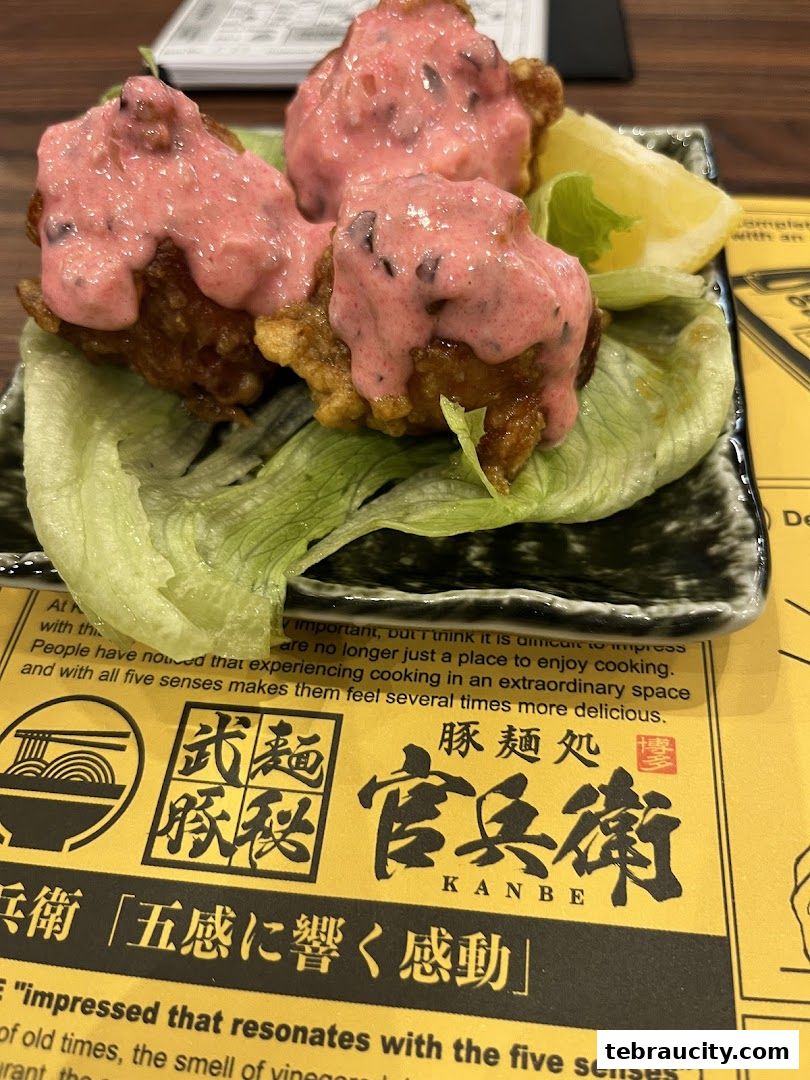 A close-up of fried chicken pieces topped with a pink sauce and served with a lemon wedge.
