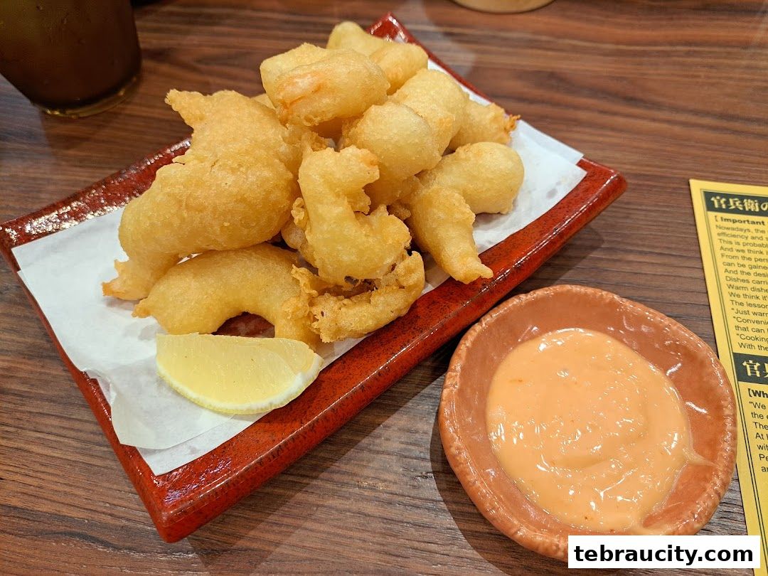 A plate of golden fried shrimp with a side of dipping sauce and a lemon wedge.