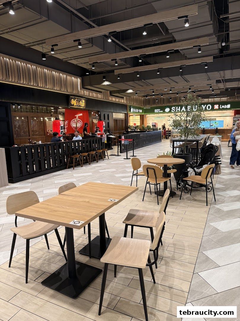 A food court area with tables and chairs, featuring a ramen shop with red lanterns.