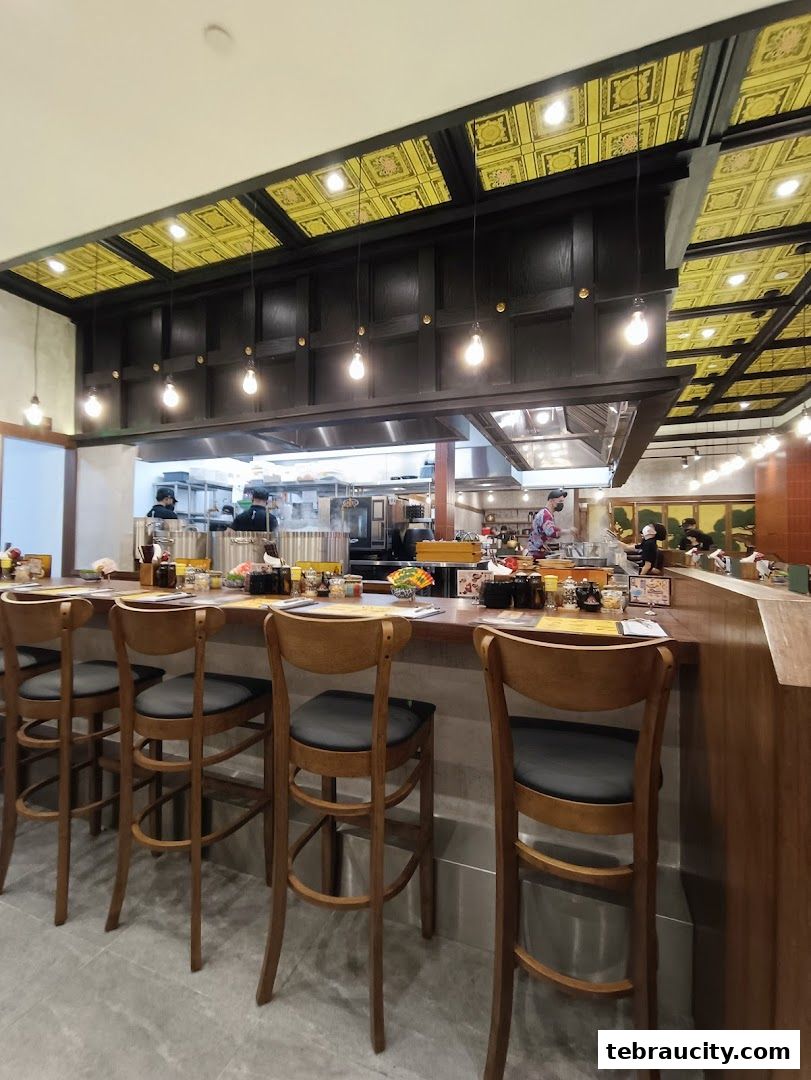 Interior view of a ramen shop with a counter, bar stools, and an open kitchen.