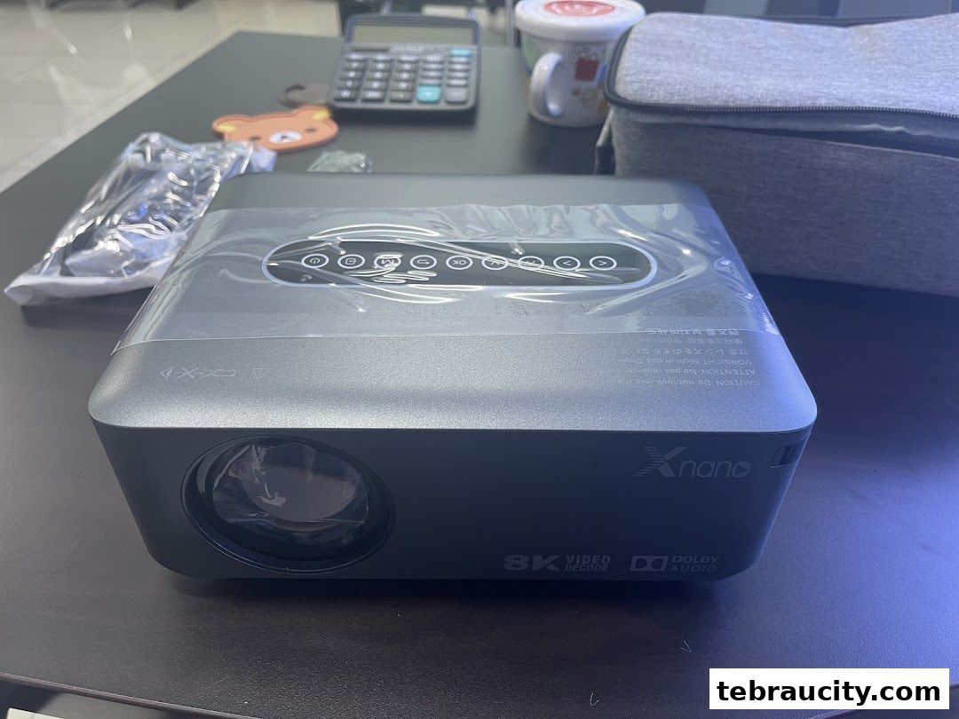 A modern projector with 'Xnano' branding and '8K Video Decode' and 'Dolby Audio' labels.