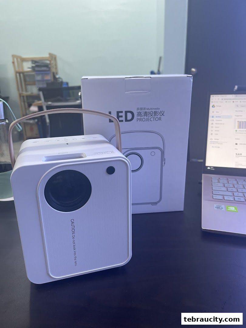 A white LED projector with a wooden handle and its box are displayed on a desk.