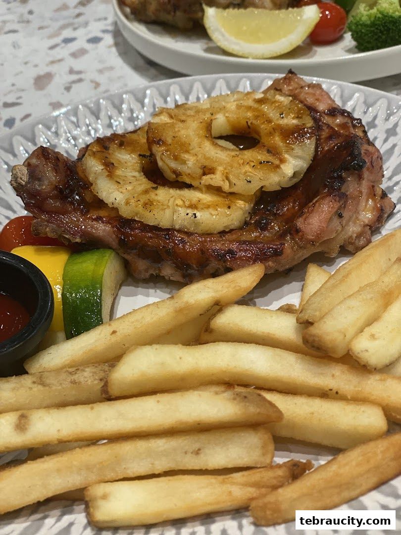 A delicious grilled pork chop topped with pineapple rings, served with fries and vegetables.