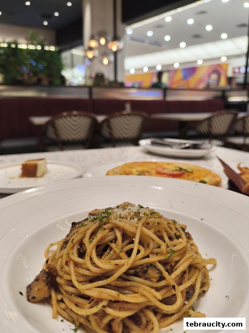 A close-up of a delicious spaghetti dish with a pizza and dessert in the background.