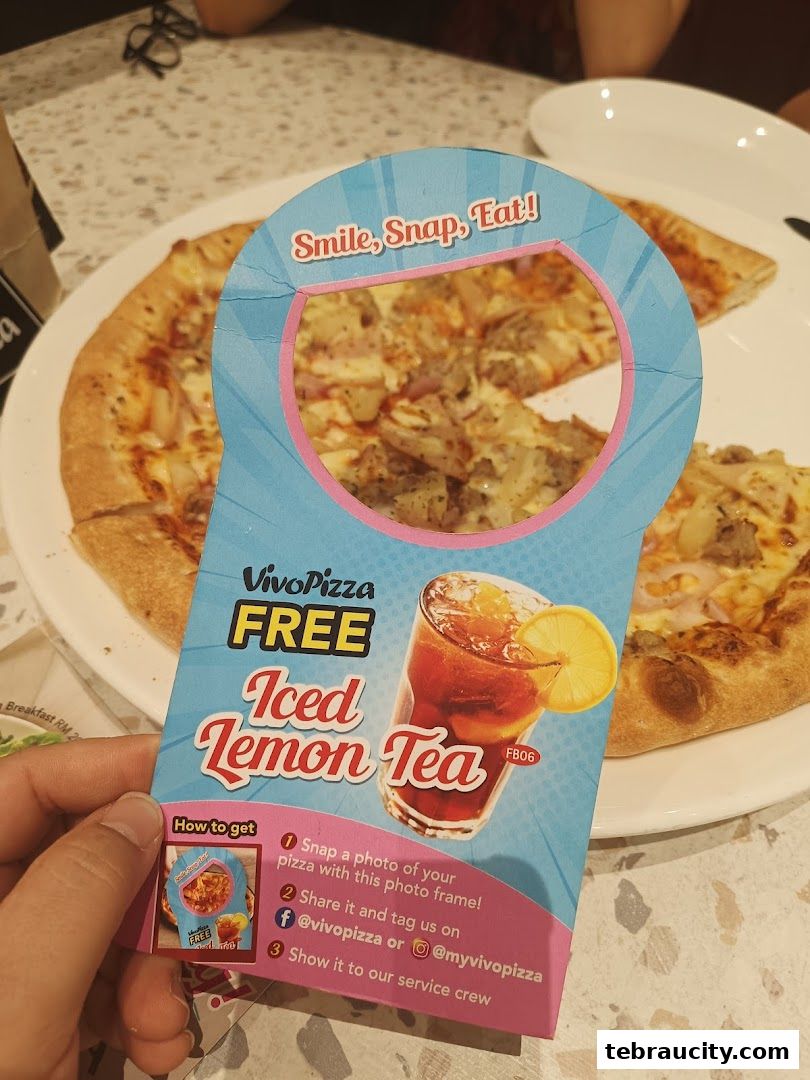 A hand holds a promotional flyer for Vivo Pizza offering a free iced lemon tea with a pizza photo.