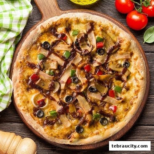 A delicious pizza topped with chicken, mushrooms, olives, and peppers on a wooden board.