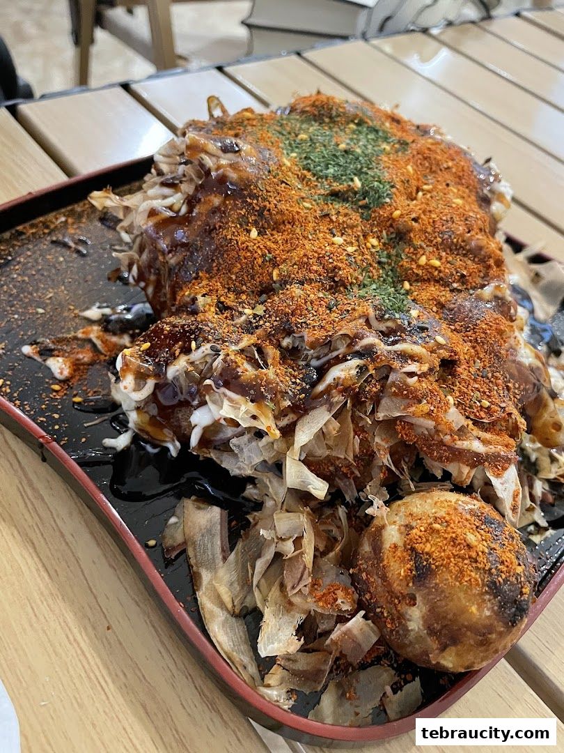 A close-up of a delicious okonomiyaki dish topped with sauce, bonito flakes, and spices.