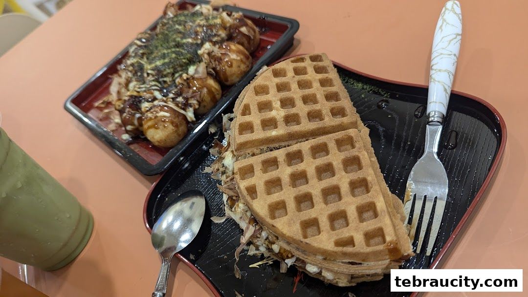 A waffle sandwich and takoyaki are served with a green drink and cutlery.