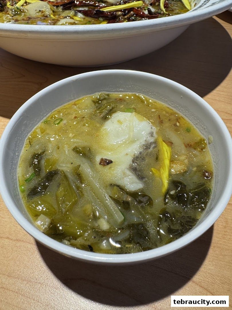 A close-up of a bowl of sour pickled cabbage fish soup with tender fish pieces.