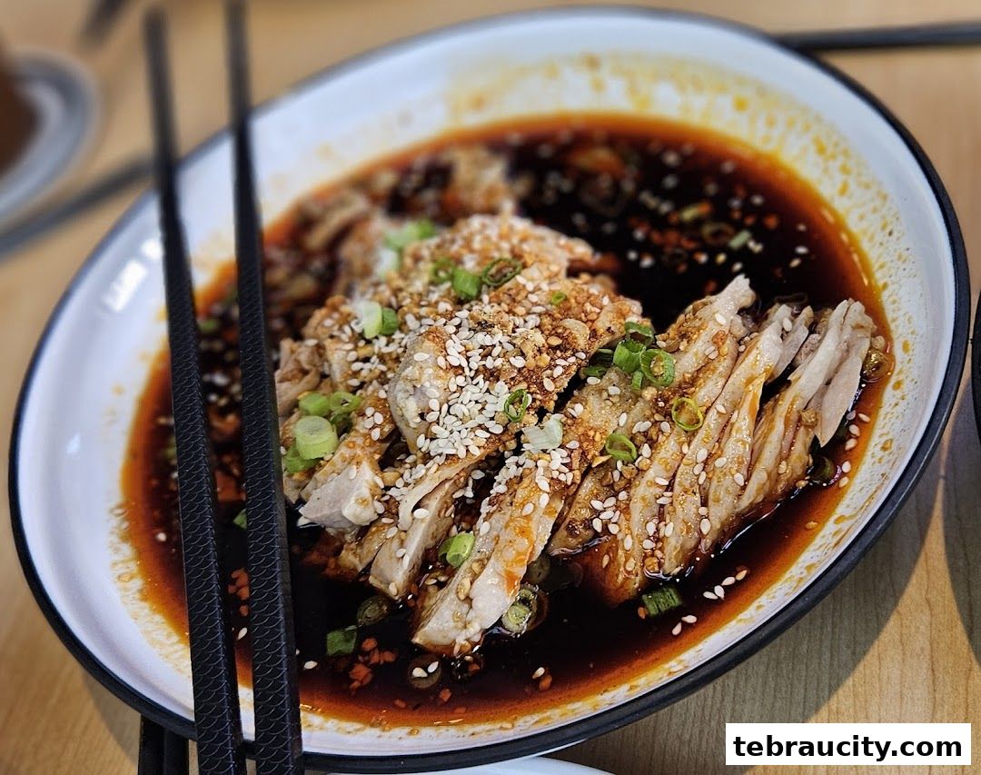 A close-up shot of a delicious dish with sliced chicken, chili oil, sesame seeds, and chopped scallions.