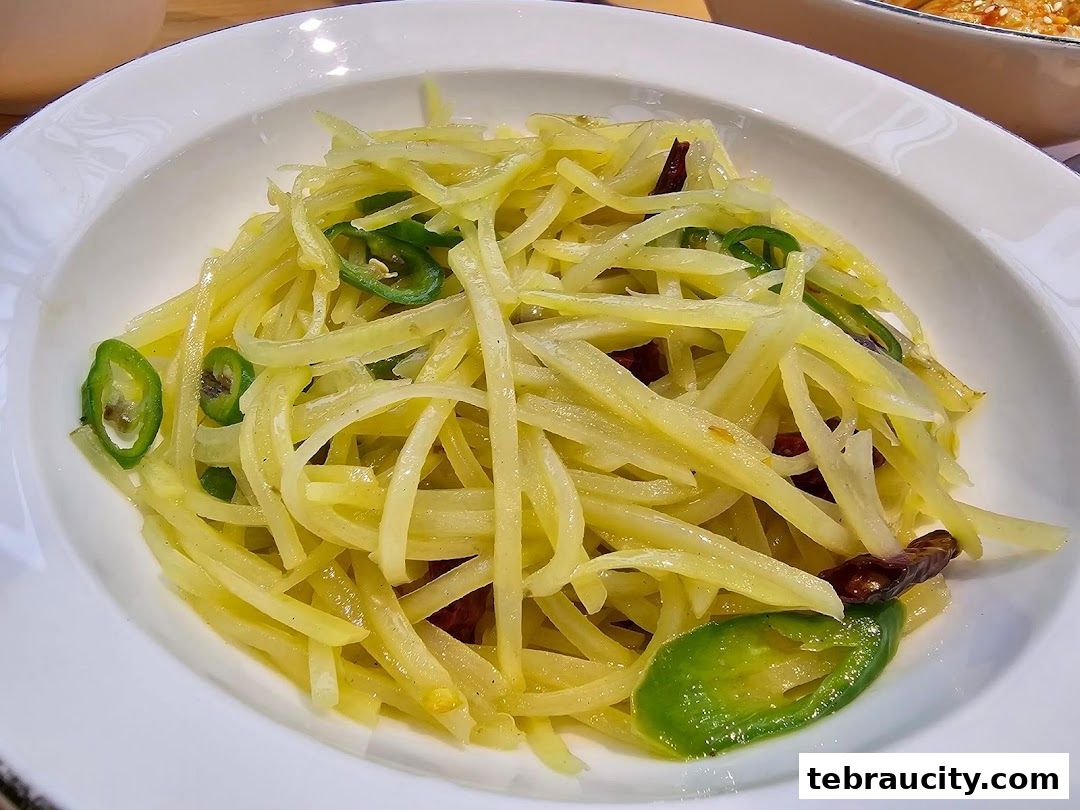 A close-up of a white bowl filled with shredded potatoes, green chilies, and dried chilies.