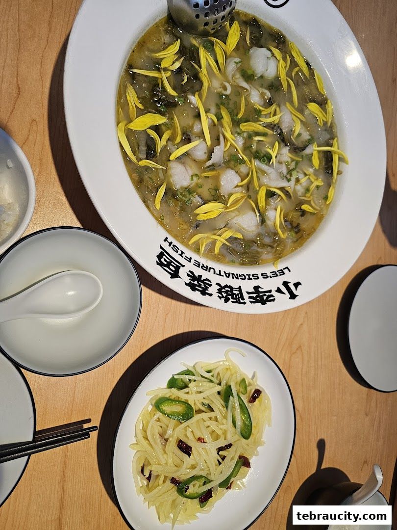 A close-up of a delicious sour fish dish with pickled vegetables and a side of stir-fried shredded potatoes.