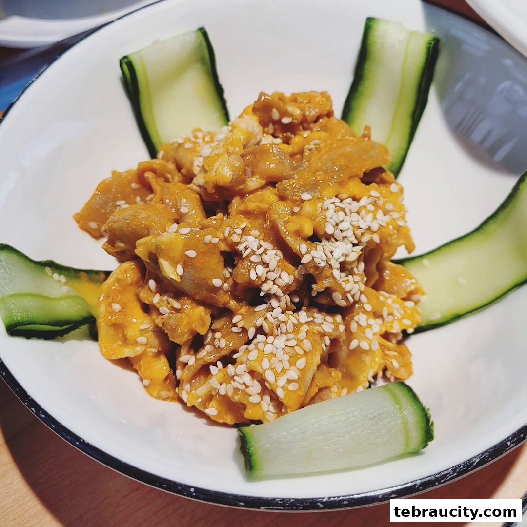 A close-up of a savory dish with shredded meat, sauce, and sesame seeds, garnished with cucumber slices.