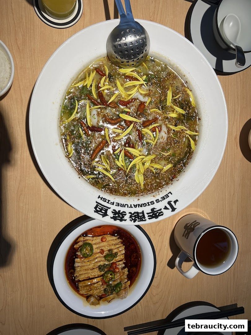 A top-down view of a delicious Sichuan-style fish dish with chili and herbs, served with a side dish and tea.