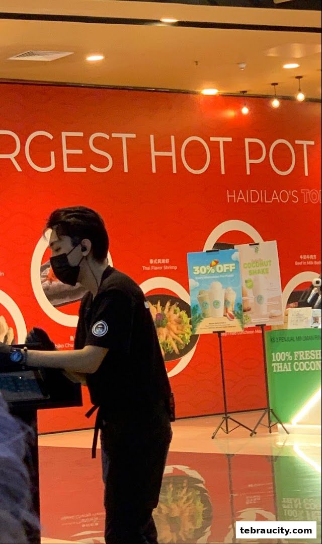 A staff member stands in front of a red wall with text and images of food.