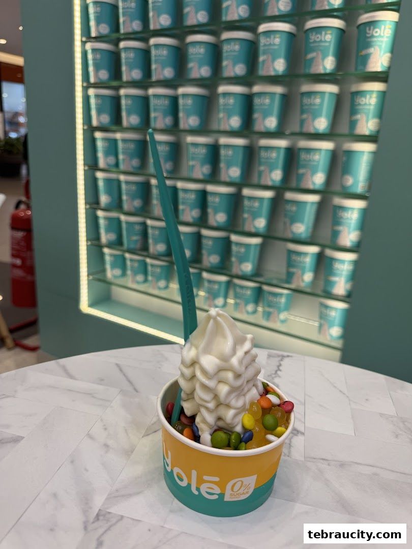 A cup of frozen yogurt with toppings and a wall of yogurt cups in the background.