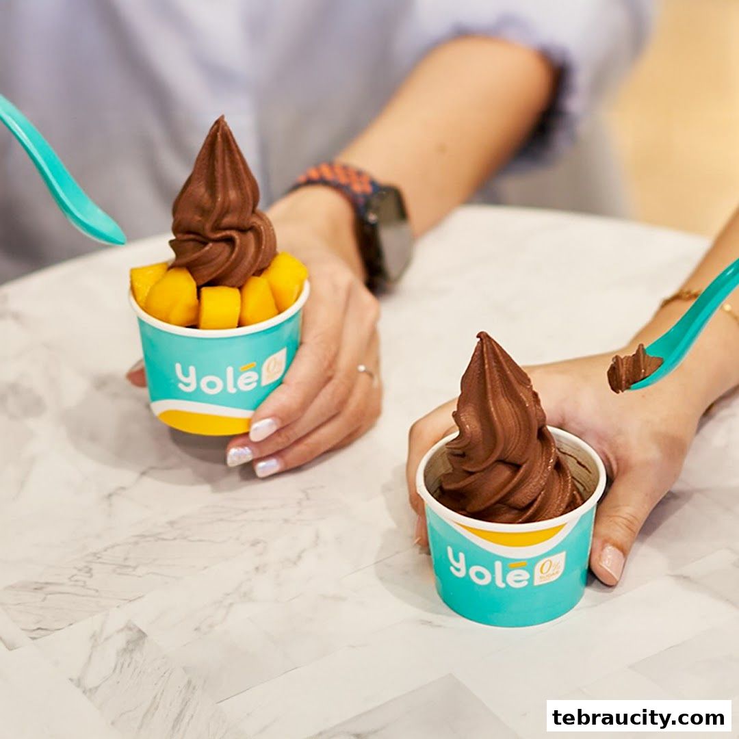 Two cups of chocolate frozen yogurt with mango chunks, being enjoyed with spoons.