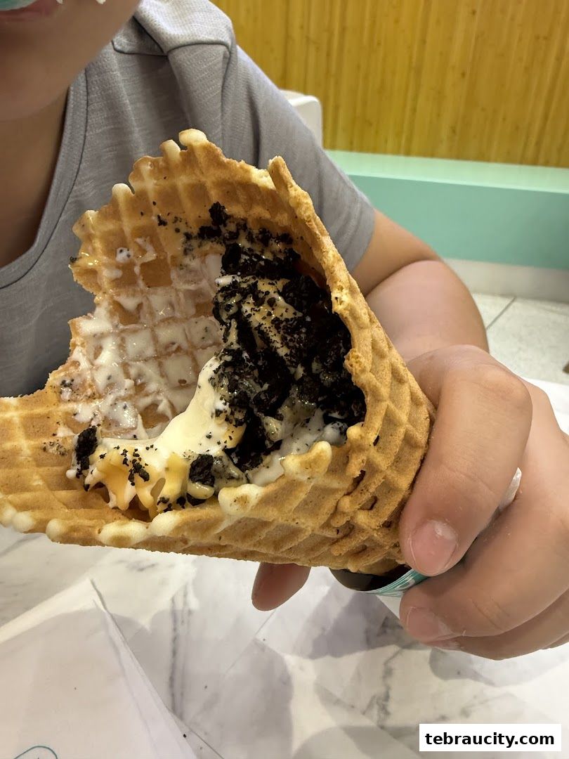 A person holding a waffle cone filled with ice cream and cookie crumbles.