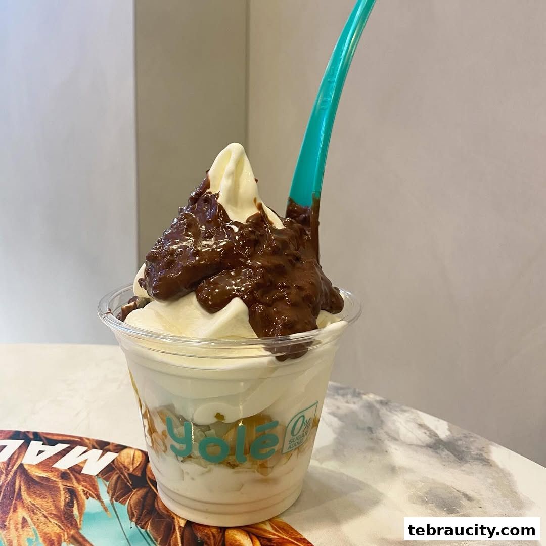 A cup of frozen yogurt with chocolate sauce and a teal spoon.