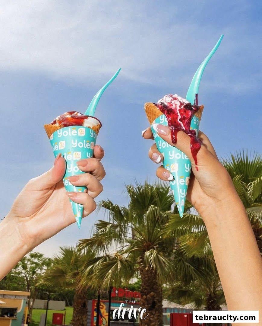 Two hands holding Yolé ice cream cones with berry toppings against a blue sky.