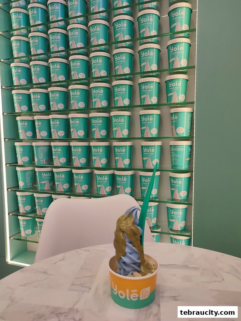 A wall display of Yolé frozen yogurt cups with a cup of blue and green yogurt in the foreground.